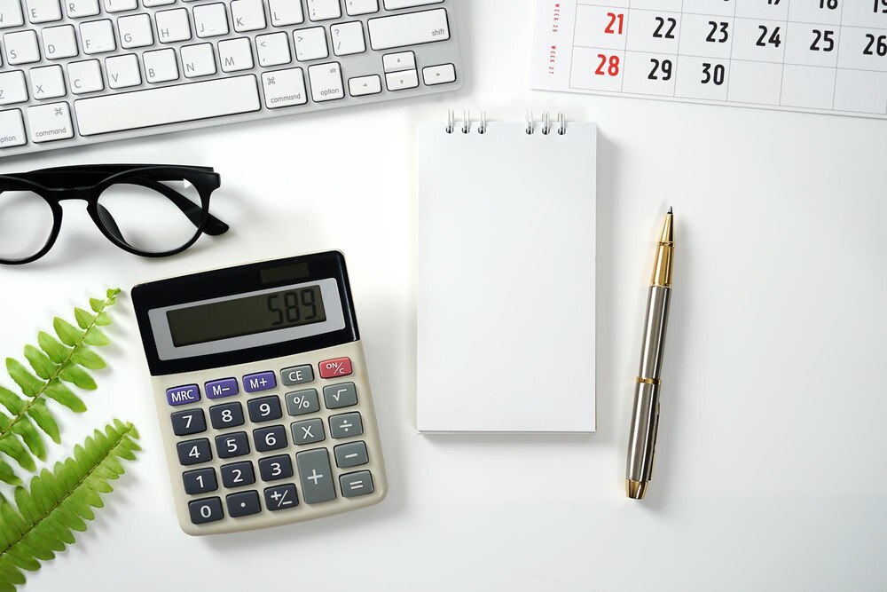 Calculadora, bloco de notas, caneta e teclado sobre uma mesa branca de escritório